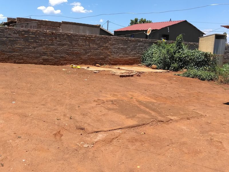A large, undeveloped rear yard area featuring a brick boundary wall and an exposed concrete slab, offering significant potential for landscaping or outdoor development.