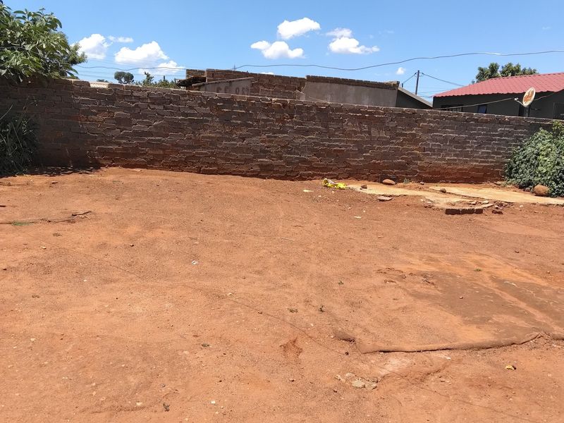 An open, undeveloped backyard area featuring a brick boundary wall, offering a blank canvas for landscaping or outdoor development.