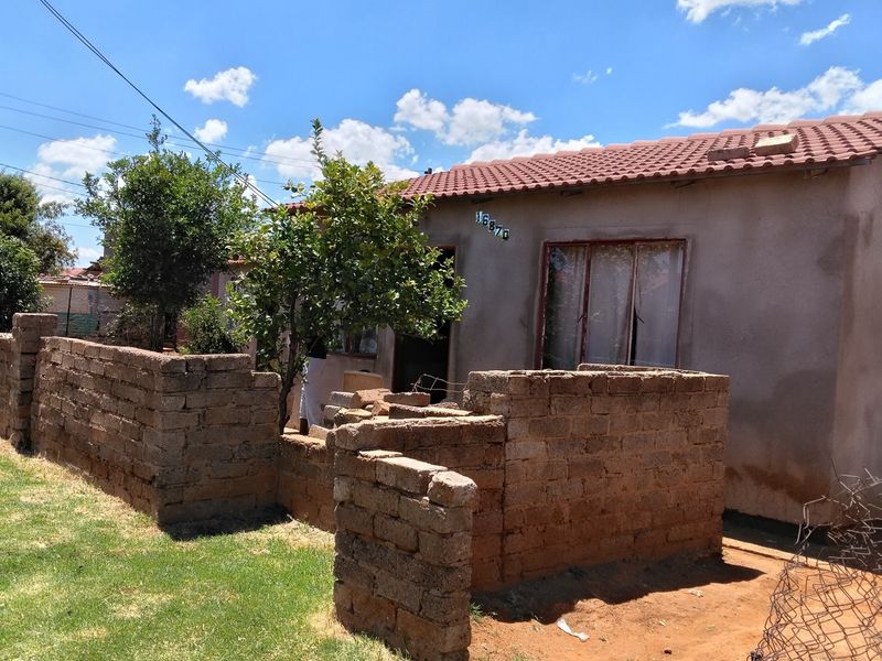 Front view of a single-story house featuring a tiled roof, metal window frames, and an unfinished brick boundary wall in the front yard.