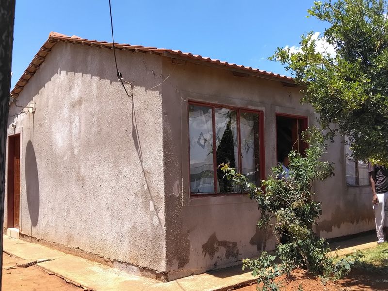 Exterior view of a single-story house featuring a tiled roof and plastered walls, showing signs of significant wear and maintenance requirements.