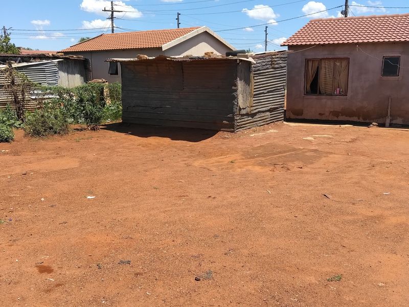 Rear yard area featuring a small corrugated iron outbuilding, adjacent to a residential structure with a tiled roof and plastered exterior walls.