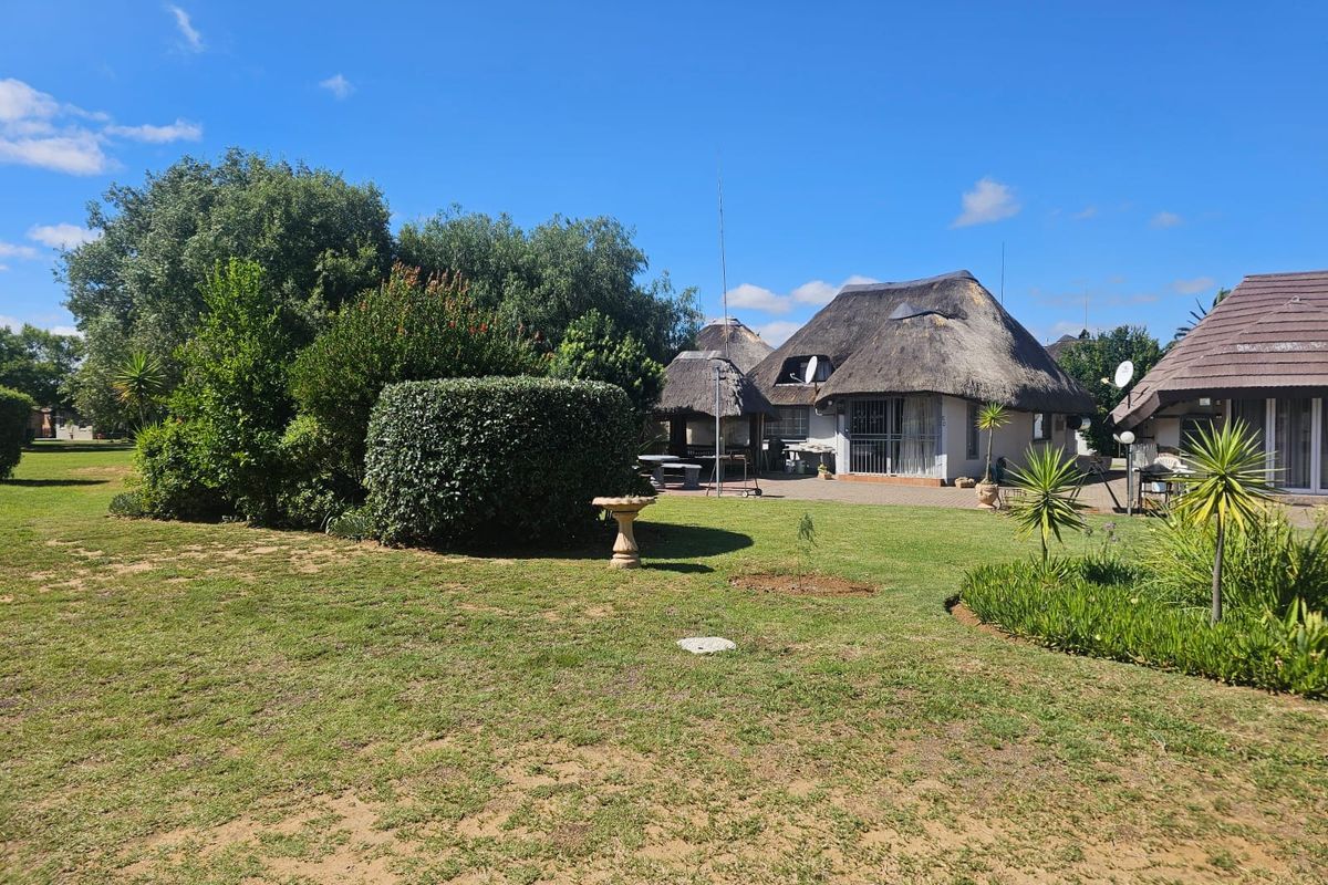 A view of the rear exterior featuring a thatched roof dwelling, a paved patio area, and a well-maintained garden.