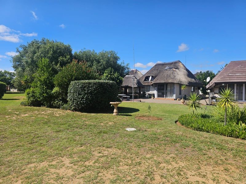 A view of the rear exterior featuring a thatched roof dwelling, a paved patio area, and a well-maintained garden.