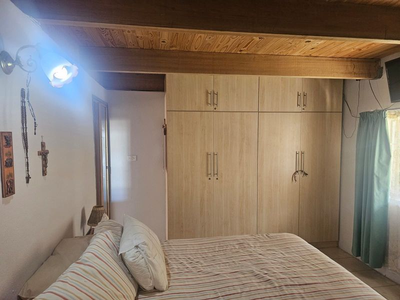 A bedroom featuring built-in cupboards and exposed timber ceiling beams, providing a functional and rustic aesthetic.