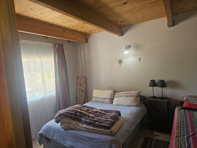 A bedroom featuring exposed timber ceiling beams, tiled flooring, and a wall-mounted light fixture, offering a rustic aesthetic.