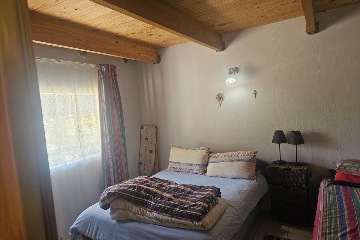 A bedroom featuring exposed timber ceiling beams, tiled flooring, and a wall-mounted light fixture, offering a rustic aesthetic.