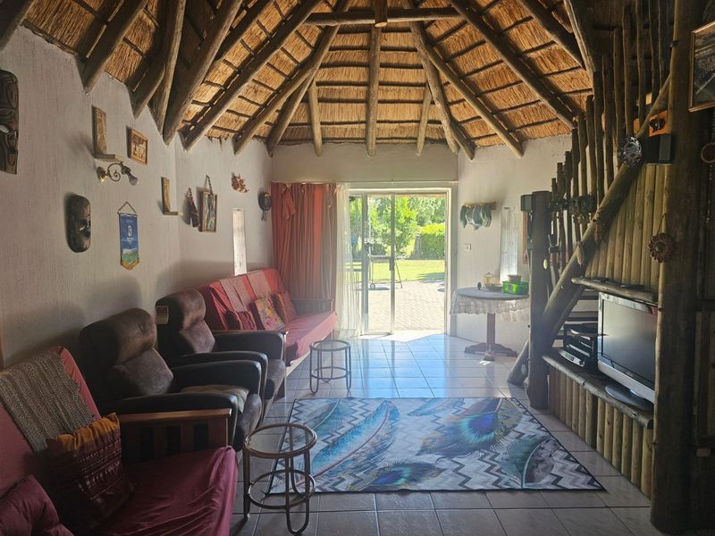 Living room featuring a traditional thatched roof with exposed timber rafters, tiled flooring, and direct access to the garden through a sliding glass door.
