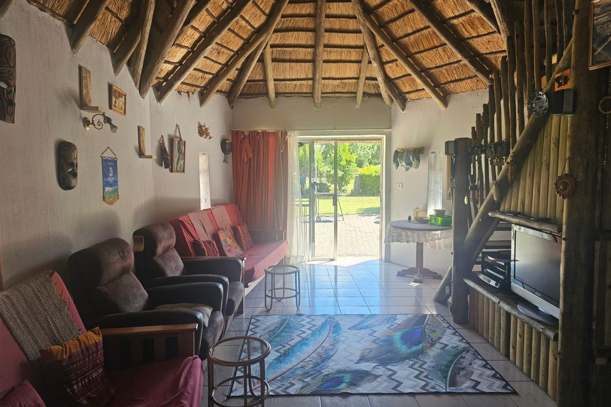 Living room featuring a traditional thatched roof with exposed timber rafters, tiled flooring, and direct access to the garden through a sliding glass door.