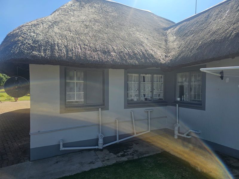 Rear exterior view of a house featuring a traditional thatch roof and exposed exterior plumbing along the wall base.