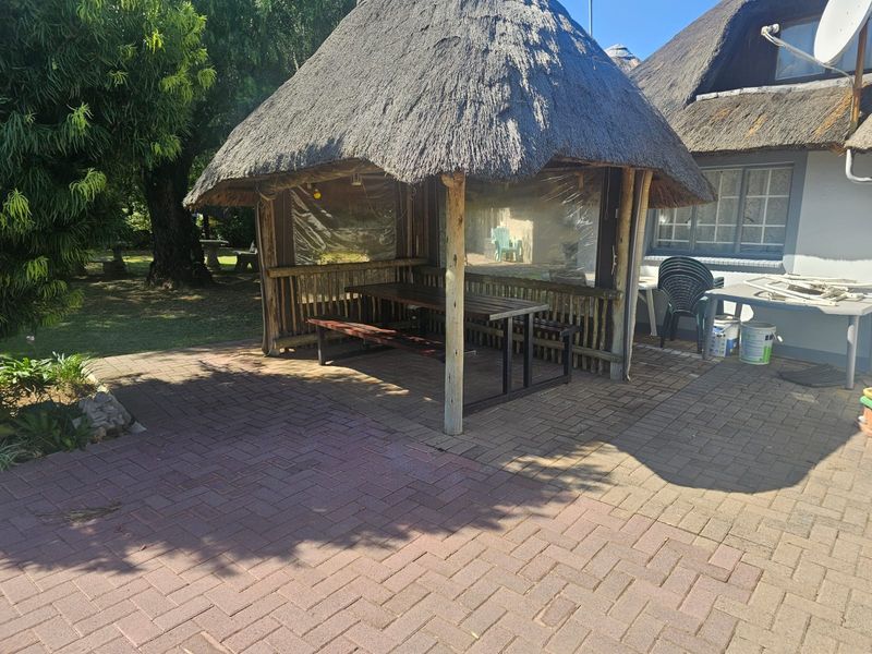 Outdoor paved patio area featuring a traditional thatch roof lapa, providing a shaded space for outdoor dining and relaxation.