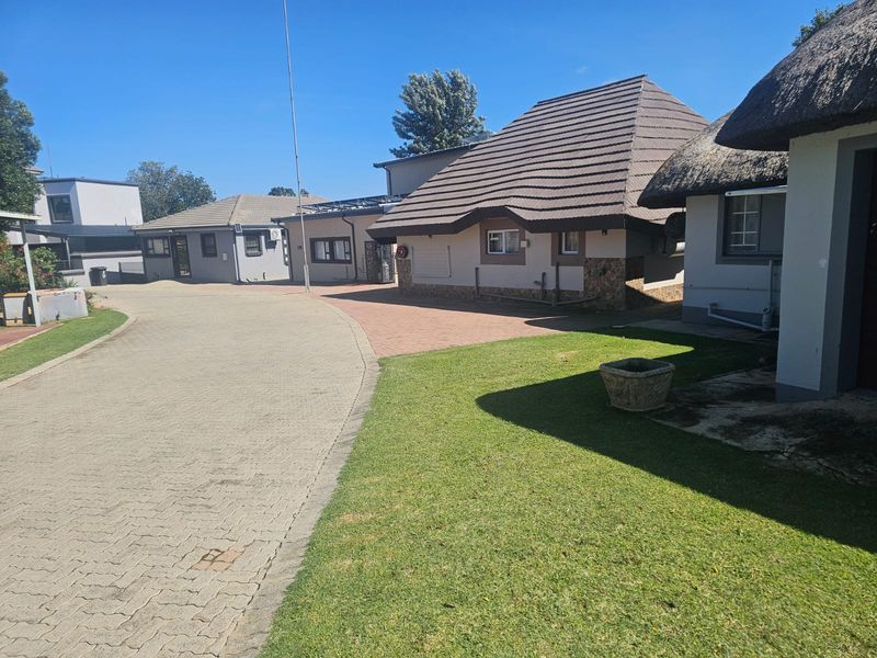 A view of the property exterior featuring a paved driveway, well-maintained lawn, and a mix of tiled and thatched roof structures.