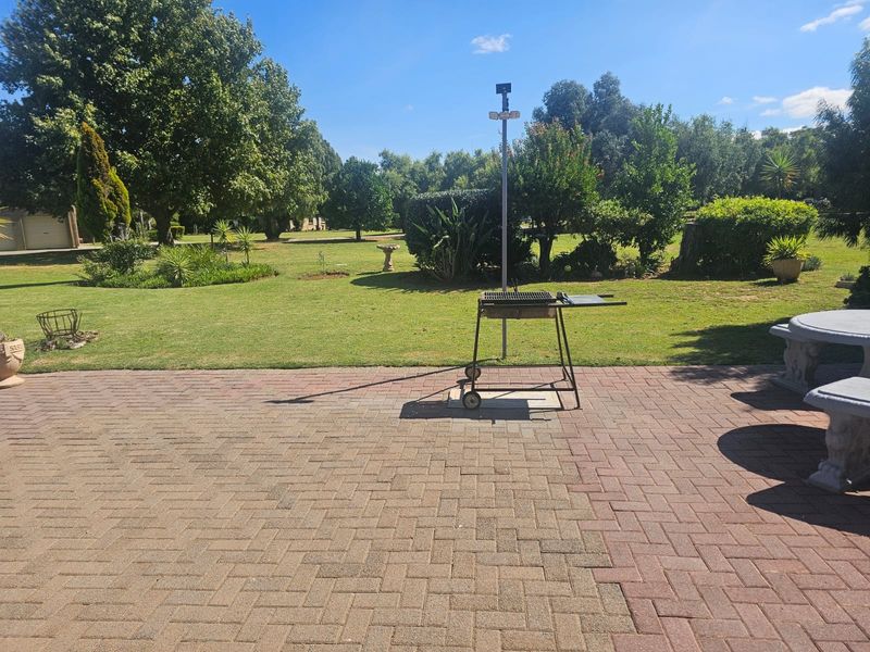 A spacious outdoor patio area featuring brick paving, overlooking a large, well-maintained garden with mature trees and established landscaping.