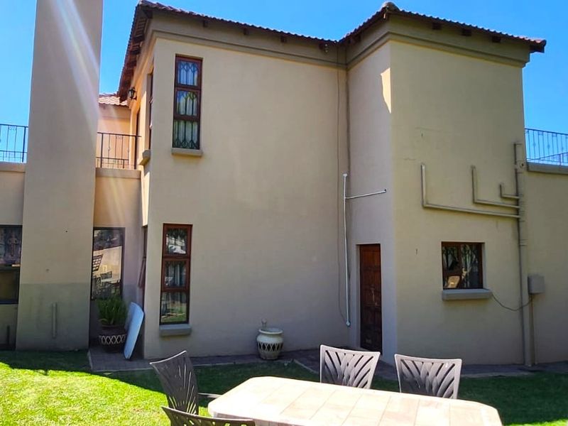 Rear view of a two-story residential property featuring a garden, paved patio area, and upper-level balcony access.