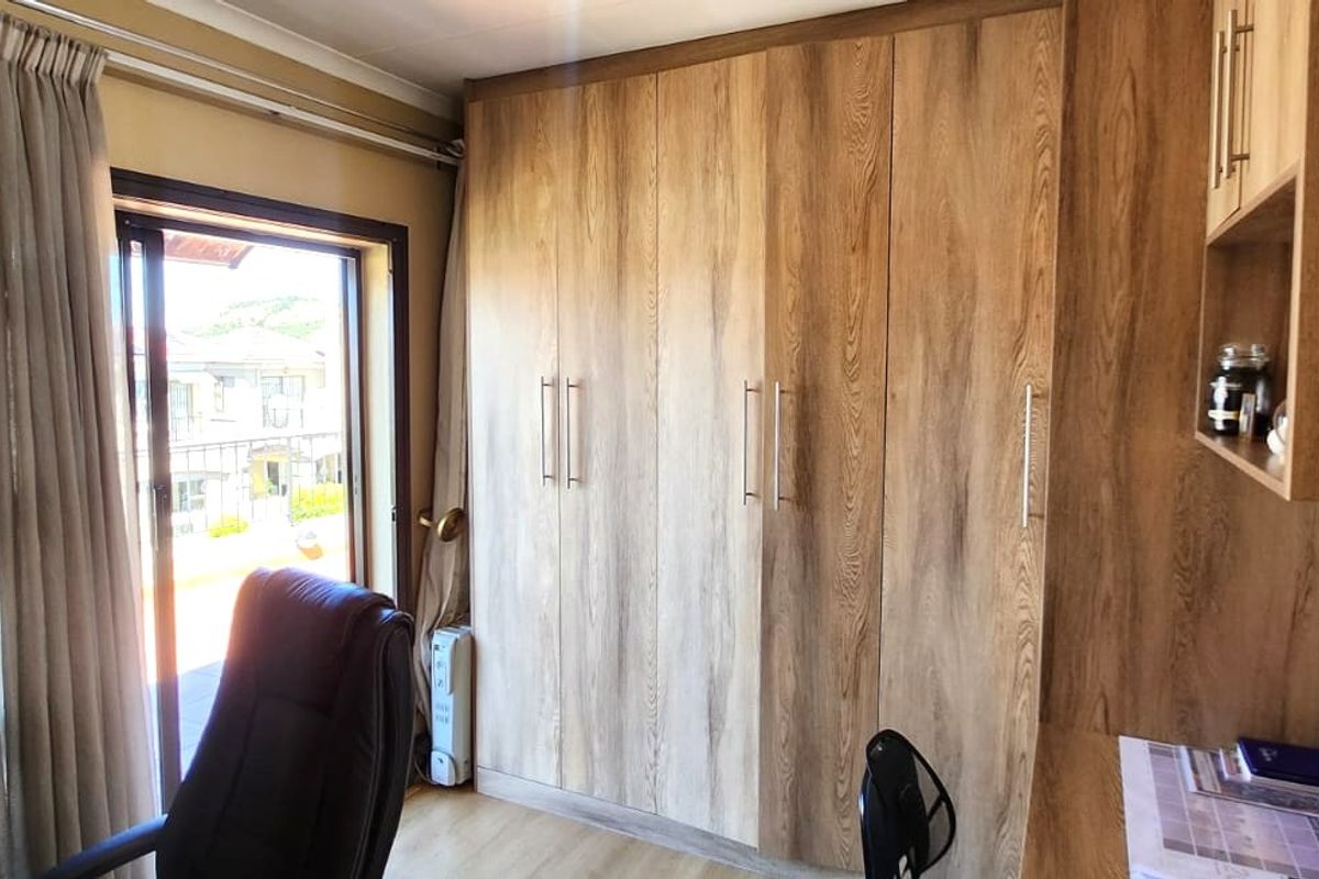 A well-maintained bedroom featuring extensive built-in wooden cabinetry, a built-in desk, laminate flooring, and a sliding door providing natural light.