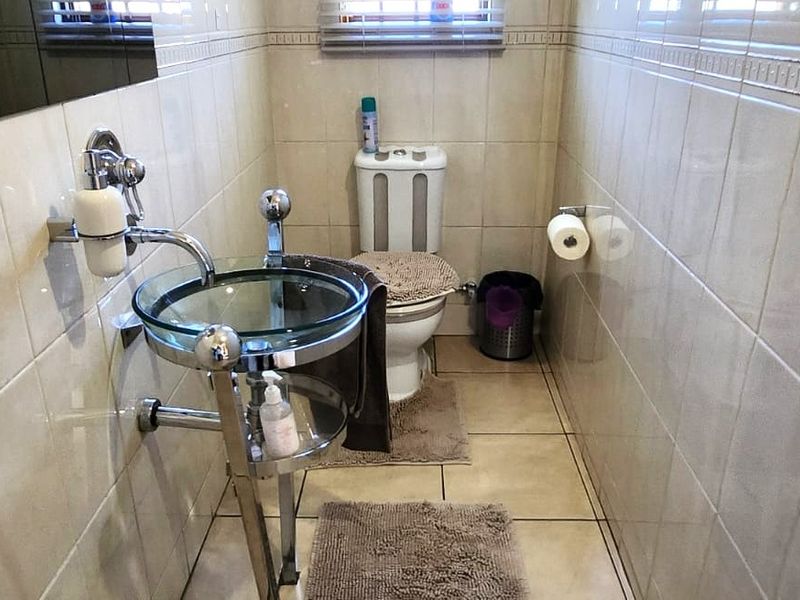 A compact guest bathroom featuring full-height wall tiling, a modern glass vessel sink with chrome fixtures, and a standard ceramic toilet.