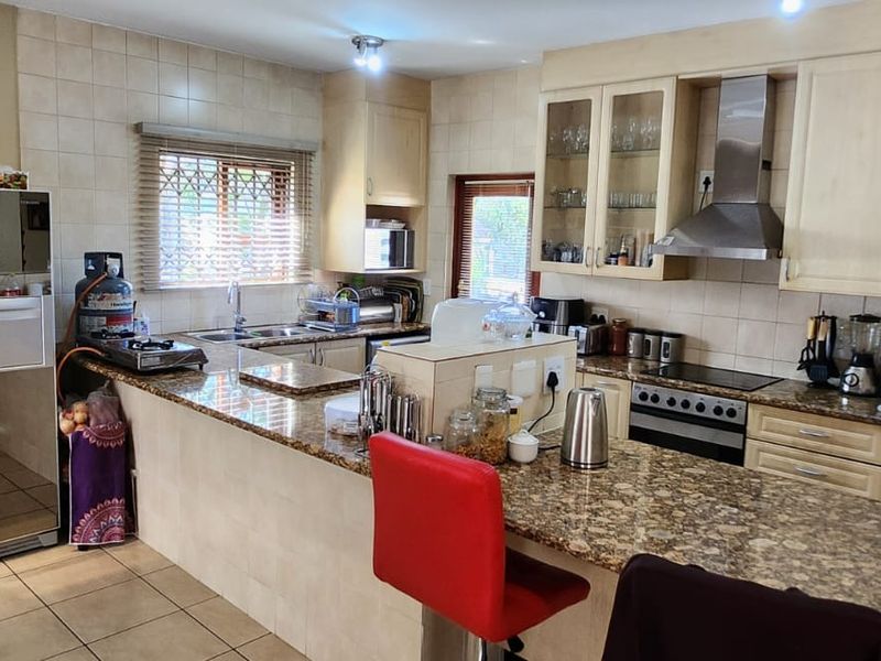 A functional kitchen featuring granite countertops, built-in cabinetry, a stainless steel extractor fan, and a tiled backsplash with a breakfast bar area.