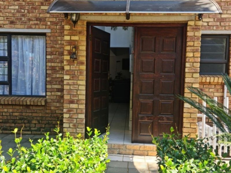 Front entrance of a face brick house featuring double timber doors, a protective canopy, and a paved walkway leading to the main entry.
