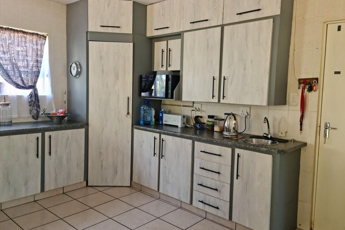 A functional kitchen featuring light wood-grain cabinetry, dark laminate countertops, tiled flooring, and ample built-in storage space.