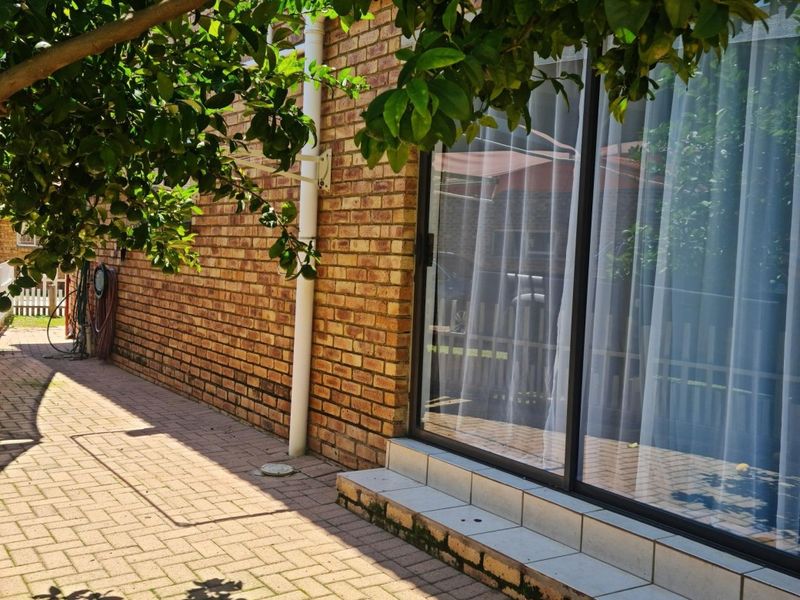 A rear exterior view showing a brick facade, paved patio area, and a sliding glass door leading into the home.