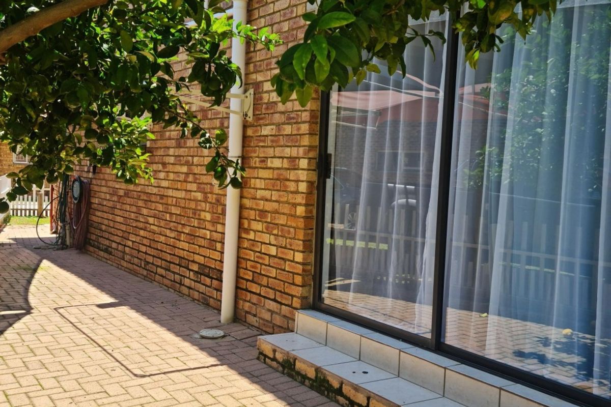 A rear exterior view showing a brick facade, paved patio area, and a sliding glass door leading into the home.