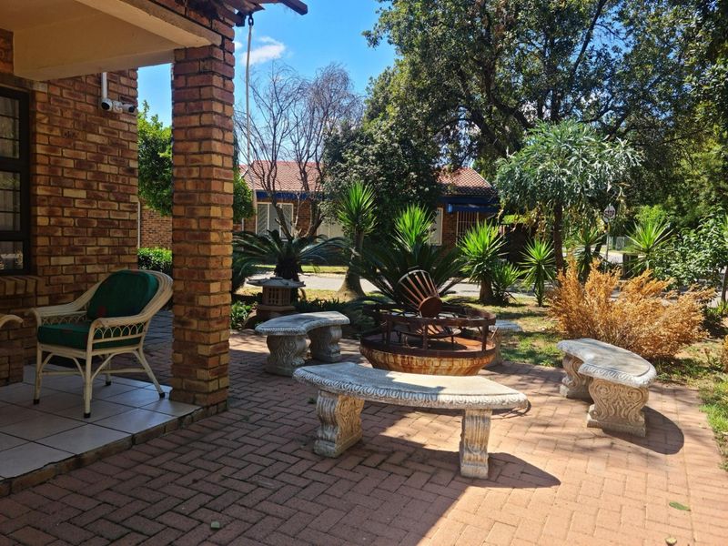 A covered brick patio area featuring brick pillars and paved flooring, overlooking a landscaped garden with mature trees and shrubs.