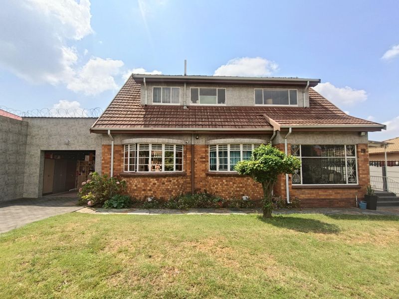 Front elevation of a double-story brick house featuring a tiled roof, dormer windows, bay windows, and a paved driveway with security fencing.