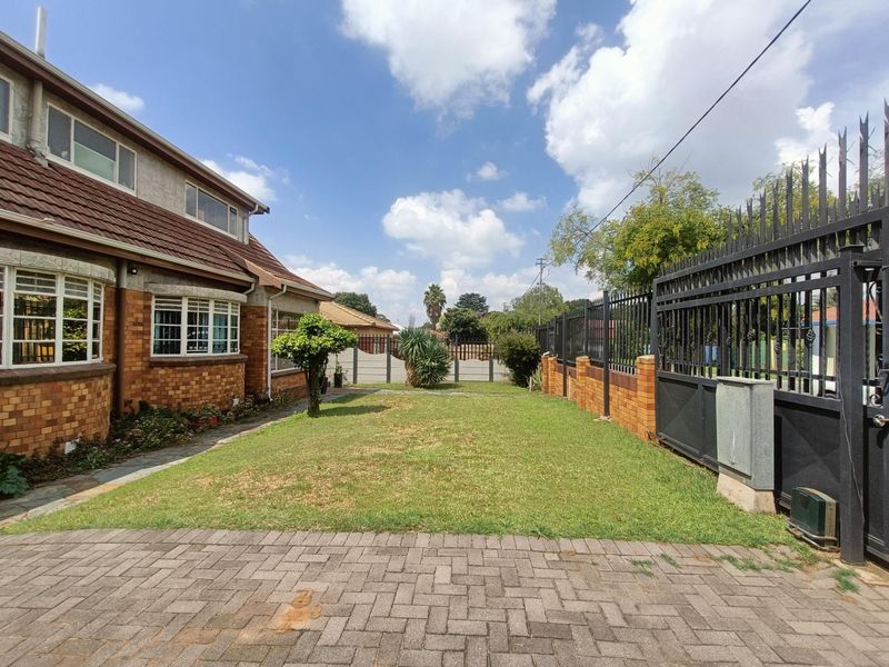 Front exterior view of the house featuring a brick facade, tiled roof, paved driveway, and secure metal perimeter fencing with a sliding gate.