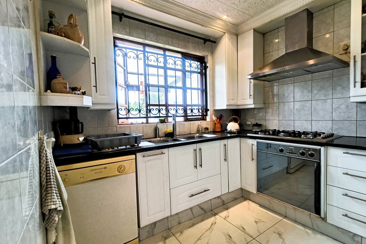 A functional kitchen featuring white cabinetry, a gas hob with extractor fan, tiled backsplash, and marble-look flooring with security bars on the window.
