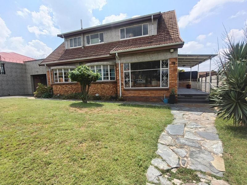 A charming double-story brick house featuring a tiled roof, a stone-paved walkway, and a covered patio area set within a well-maintained front garden.