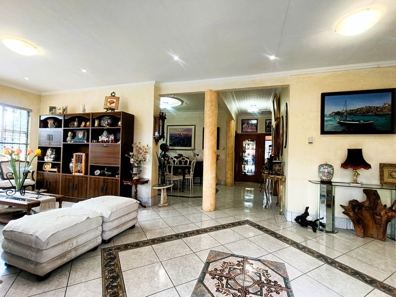 Spacious open-plan living area featuring tiled floors with decorative inlay, structural columns, and recessed lighting, creating a connected flow between living and dining spaces.