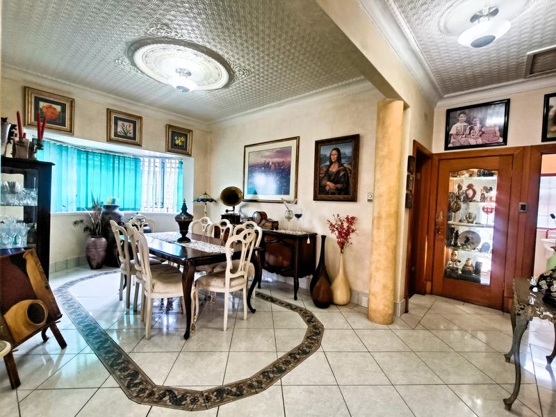 Spacious dining room featuring decorative ceiling tiles, a central ceiling rose, ceramic flooring with a decorative inlay, and a built-in display cabinet.