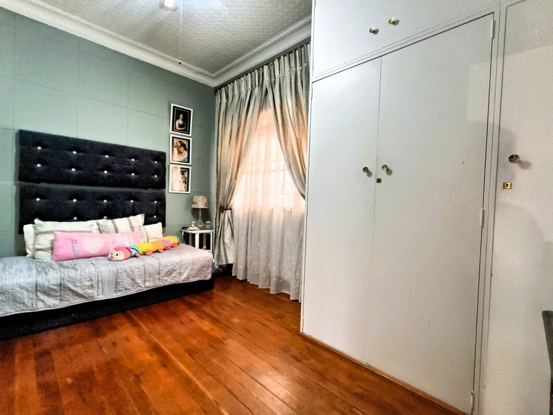 A well-maintained bedroom featuring polished hardwood flooring, a large built-in wardrobe, and decorative ceiling cornicing.