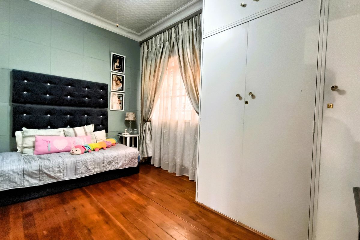 A well-maintained bedroom featuring polished hardwood flooring, a large built-in wardrobe, and decorative ceiling cornicing.