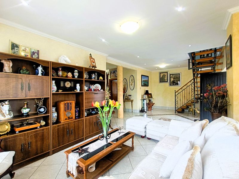 Spacious living area featuring tiled flooring, recessed lighting, and an open staircase with a decorative wrought iron balustrade.