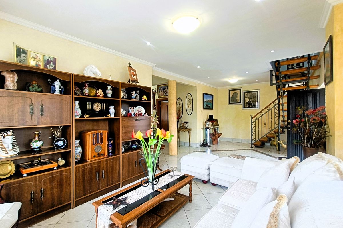 Spacious living area featuring tiled flooring, recessed lighting, and an open staircase with a decorative wrought iron balustrade.