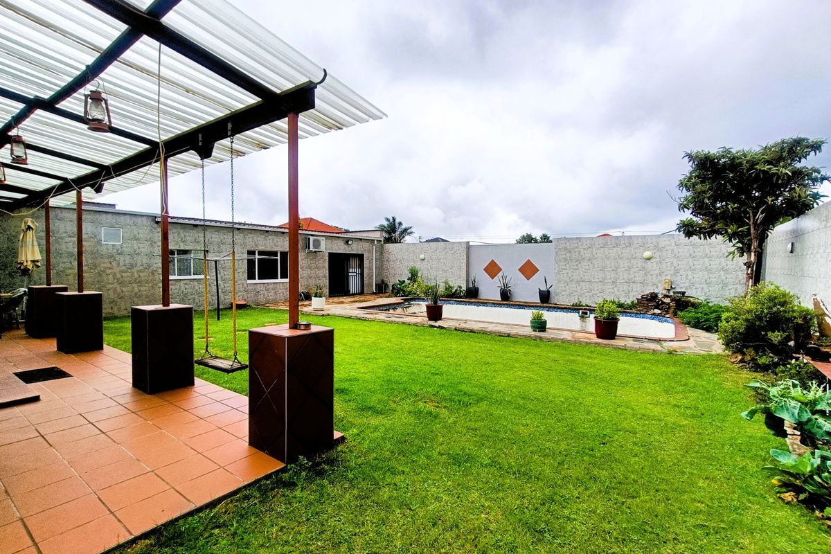 Spacious rear garden featuring a swimming pool, a covered patio area with tiled flooring, and a secure perimeter wall.