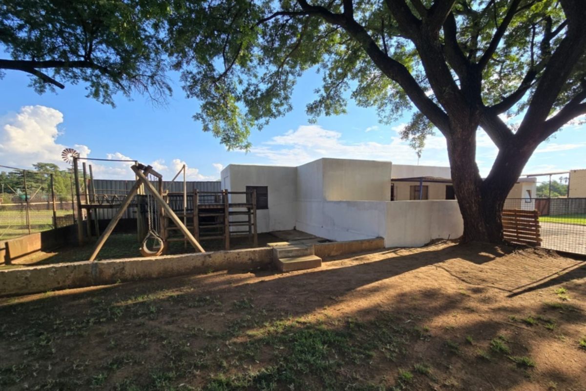 Rear exterior view of the property featuring a large mature tree, retaining wall, and fenced outdoor area.