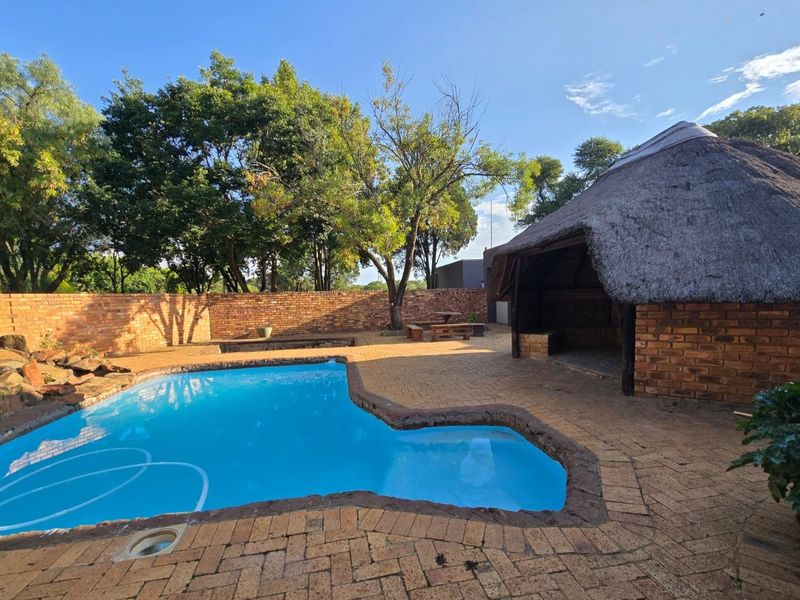 Outdoor entertainment area featuring a swimming pool, brick paving, and a traditional thatched lapa structure set within a private garden.