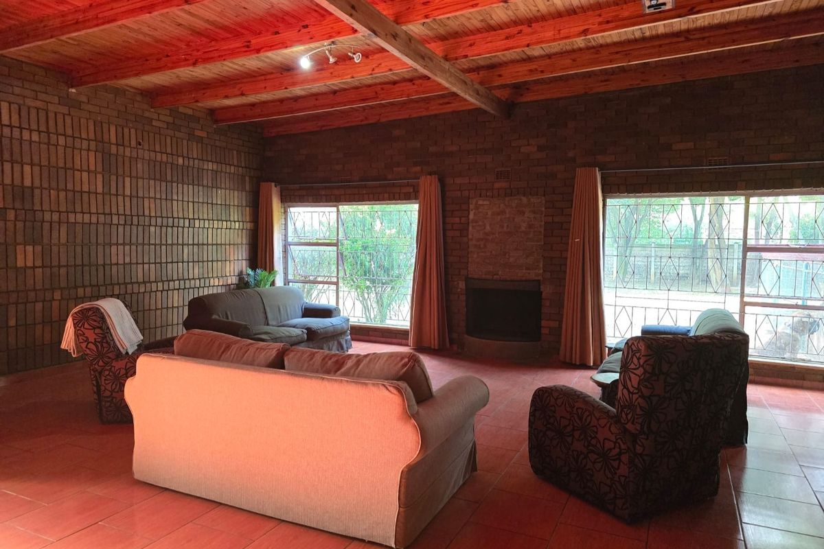 Spacious living room featuring rustic facebrick walls, a high exposed timber beam ceiling, tiled flooring, and a built-in fireplace with large windows.