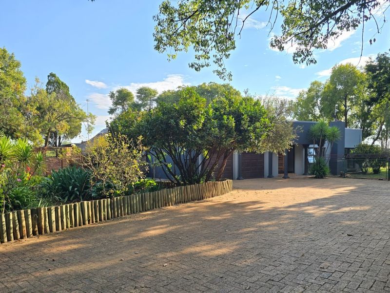 Front view of the property featuring a paved driveway, established garden with timber edging, and a covered entrance leading to the garage area.