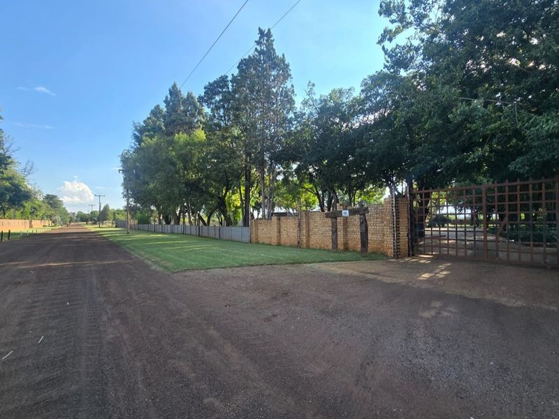 Street view of the property entrance featuring a brick boundary wall, metal gate, and established trees along the perimeter.