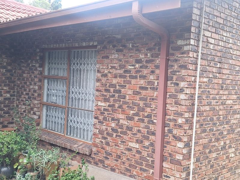 A view of the rear exterior facade featuring face brick walls, tiled roofing, and installed security gates on the windows.