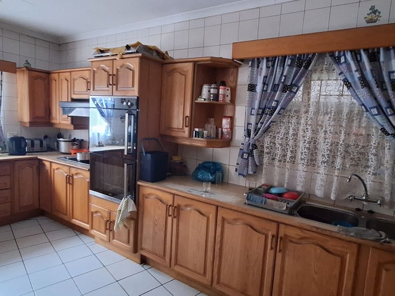 A functional kitchen featuring traditional wooden cabinetry, integrated oven, extractor fan, and double bowl stainless steel sink with ceramic tiled walls and floors.