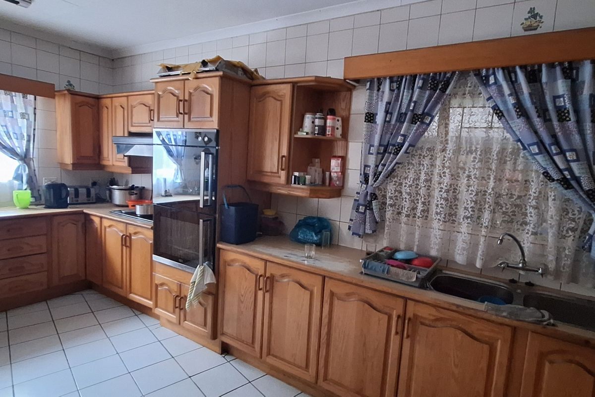 A functional kitchen featuring traditional wooden cabinetry, integrated oven, extractor fan, and double bowl stainless steel sink with ceramic tiled walls and floors.