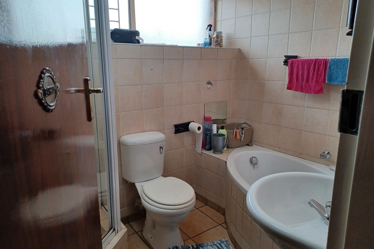 A functional bathroom featuring a pedestal basin, bathtub, and separate shower enclosure with neutral wall and floor tiling.