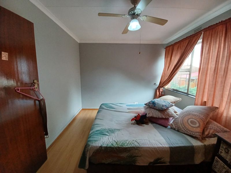 A bedroom featuring laminate flooring, a ceiling fan, and a window with curtains.