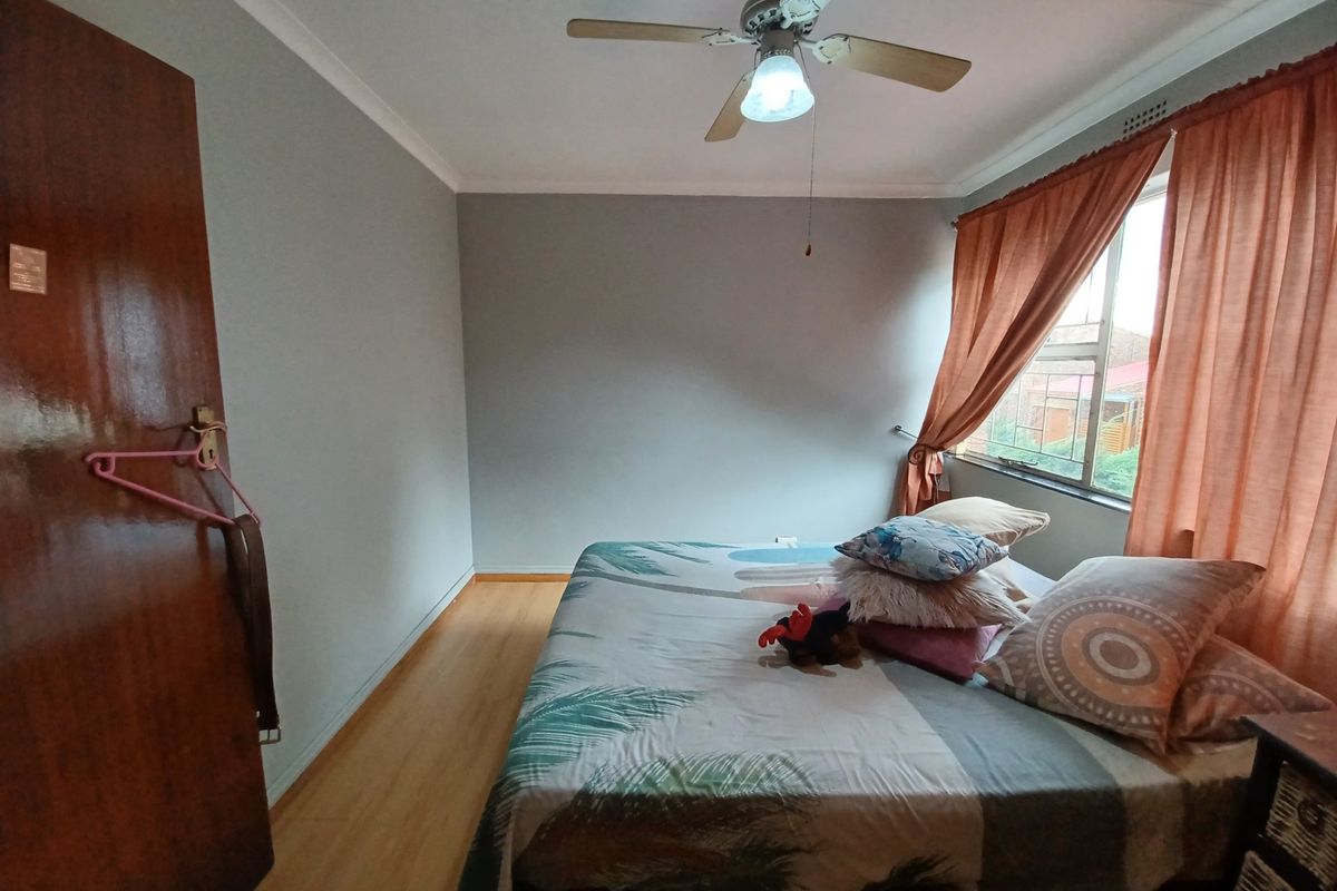 A bedroom featuring laminate flooring, a ceiling fan, and a window with curtains.