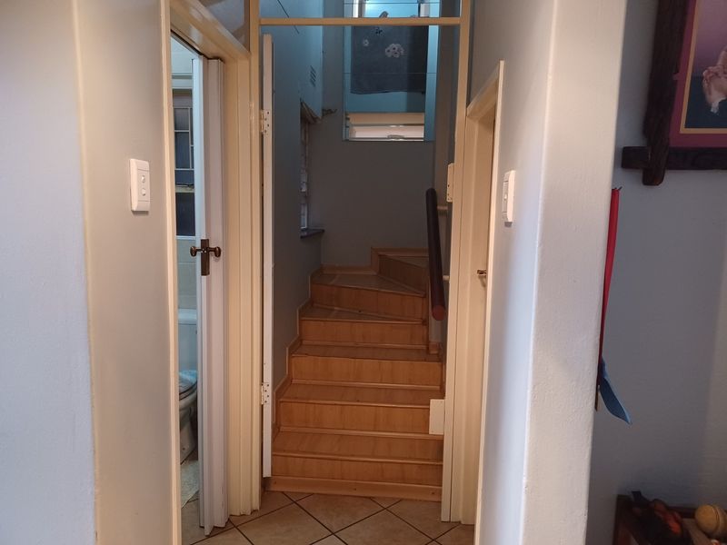 A hallway featuring a wooden staircase with a handrail, leading to an upper level, with tiled flooring and access to adjacent rooms.