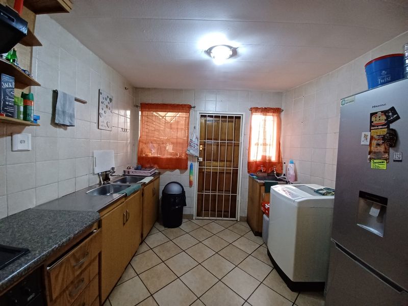 Functional kitchen featuring tiled walls and flooring, built-in cabinetry, stainless steel sink, and a secure rear entrance door.