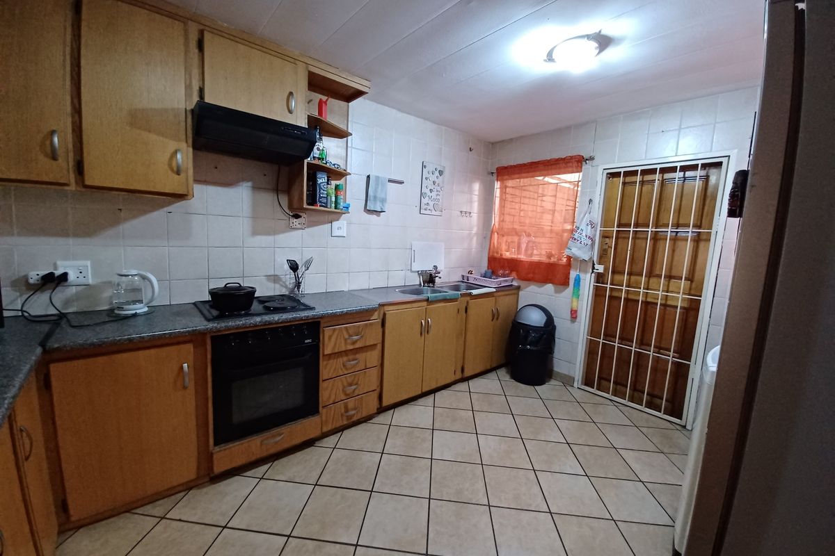 Functional kitchen featuring laminate cabinetry, built-in oven, electric hob, extractor fan, stainless steel sink, and tiled flooring with direct access to the exterior.